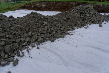 Geotextile layer between raw stones and black ground.