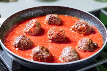 Meatballs in tomato sauce with basil on top. Bright background with ingredients in blurry background. This meal is called Kofte in Turkey and Cufte in Balkans. International meatball day.