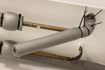 Water pipes mounted under ceiling are covered with thermal insulation.