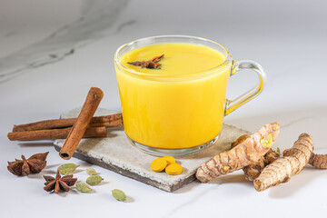 A glass cup of golden milk with turmeric powder and fresh turmeric root and anise and cinnamon on a...