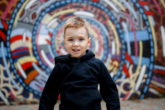 portrait of a stylish emotional baby boy in a black hoodie against the background of a colored wall in the city. concept of urban stylish clothes for children