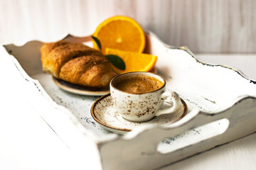 Morning breakfast coffee cup on saucer, croissant, fresh orange fruit on white shabby wooden tray