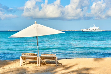 white sun lounger in front of the sea of isla mujeres in very sunny day with a yacht in the background. mexico caribbean beaches