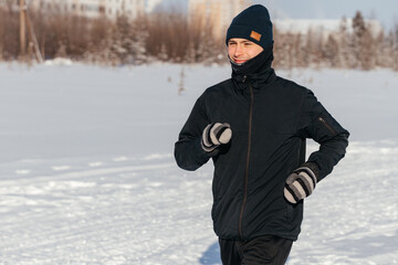 Fototapeta na wymiar Sporty young man in sportswear jogging through a snowy winter forest. Side view.Playing sports in cold weather. Concept of seasonal sports and acclimatization training