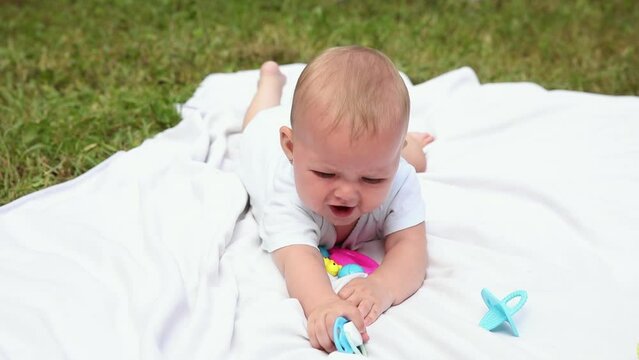 Little newborn girl lying on tummy chewing rattle on blanket, summer day outdoor. Infant having fun outdoors. Infant baby child resting playing learning to crawl. Motherhood teething, babyhood concept