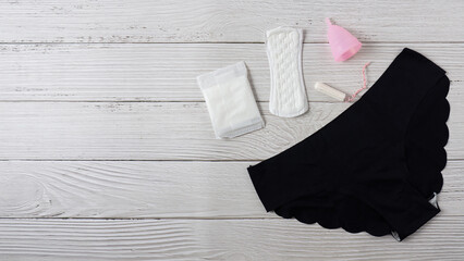 Different types of feminine menstrual hygiene materials products such as pads cloths tampons and cups with underpants. White wooden background. Banner with copy space