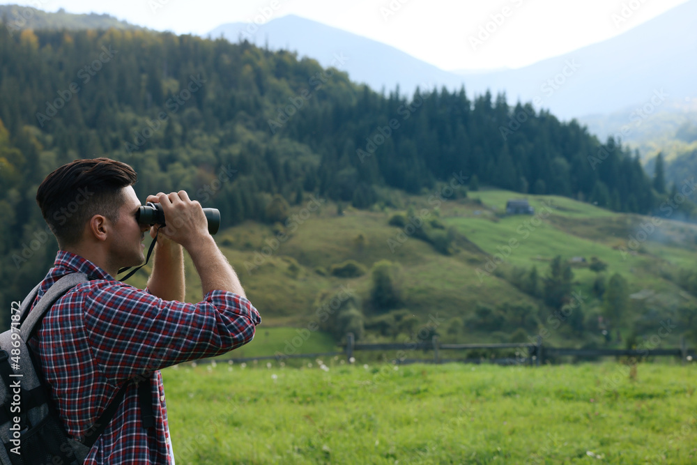 Wall mural man with backpack looking through binoculars in mountains