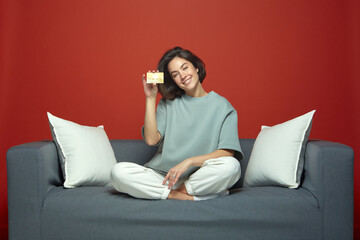 Fototapeta na wymiar Smiling young woman holding bank credit card with online service, sitting on couch. E-commerce concept