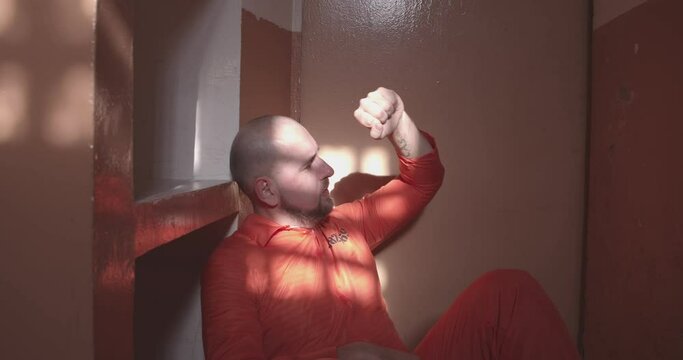 crying prisoner sits on the floor and hits his hand on the prison cell door