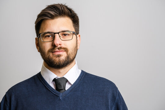 Portrait of one adult caucasian man 30 years old with beard and eyeglasses looking to the camera in front of white wall background wearing sweater young businessman success concept copy space