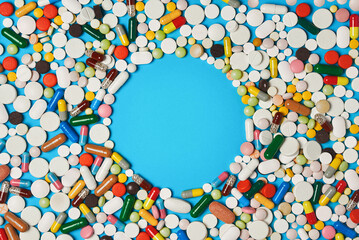 many colorful pills tablets and capsules on a blue background. Round copy space