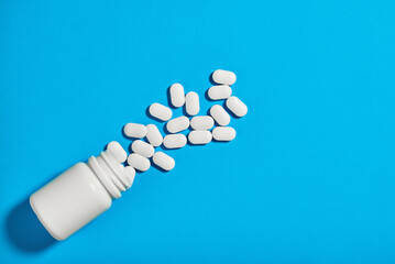 white bottle of pills lies on a blue background. The tablets are scattered side by side