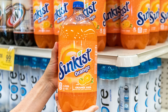 Title: Sacramento CA, USA January 4th 2022 Shoppers hand holding a plastic bottle of Sunkist orange flavored soda in a supermarket aisle. Produced by Keurig Dr Pepper in the US. 