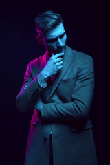 Young handsome model posing in a studio in a trendy neon light. Fashionable man in a stylish suit. Vibrant color. Bright colorful light effects. Disco style. Overlay. Gel filter. Supersaturated