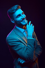 Young handsome model posing in a studio in a trendy neon light. Fashionable man in a stylish suit. Vibrant color. Bright colorful light effects. Disco style. Overlay. Gel filter. Supersaturated