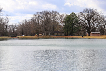 a shot of a still green lake surrounded by bare winter trees along the banks of the lake with...