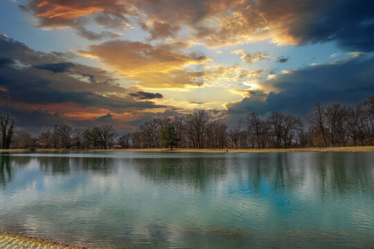 a still green lake surrounded by yellow winter grass in the park with powerful yellow and red clouds at sunset and bare winter trees at Martin Luther King Riverside Park in Memphis Tennessee USA © Marcus Jones
