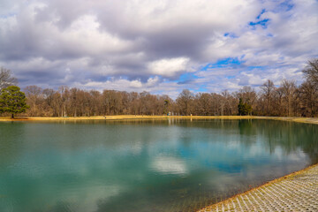 a shot of the green lake waters with bare winter trees and lush green trees on the banks of the...
