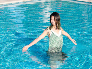 Portrait of young Asian woman standing in swimming pool and playing water, beautiful Chinese girl with green hairs in green dress enjoy sunny summer day in water.