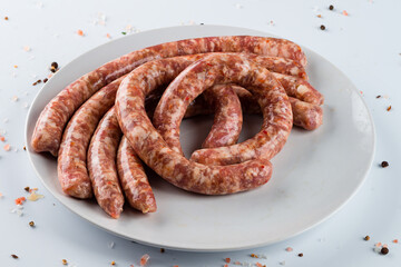Raw thin long chicken sausages on white dish