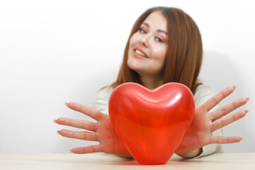 Toy red heart. Girl holds her heart in front. Holds fingers in the shape of angel wings. Valentines Day. Happy smiling young woman with  red heart shaped balloon