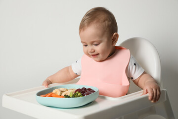 Cute little baby wearing bib while eating on white background
