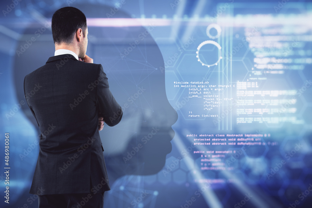 Wall mural Attractive young european businessman standing in blurry office interior with abstract glowing tech head outline hologram. Machine learning and ai concept. Double exposure.