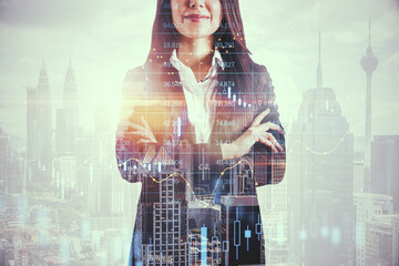 Attractive young european businesswoman with folded arms standing on bright city background with candlestick forex grid chart. Trade, finance and economy concept. Double exposure.
