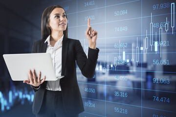 Attractive happy european businesswoman using laptop in blurry office interior with glowing forex chart and big data grid. Trade, finance and economy concept. Double exposure.