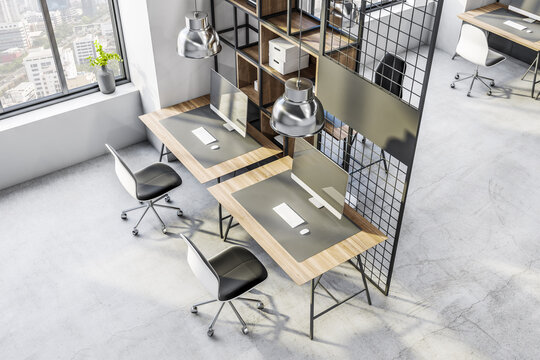 Top view on spacious work places background in loft interior design office with city view, computers on wooden table surfaces, cozy chairs, stylish chrome lamps and concrete floor. 3D rendering