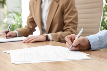 Man signing contract at table in office, closeup.