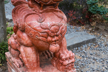 two large exotic marble red dog statues surrounded by lush green trees near a long winding footpath...