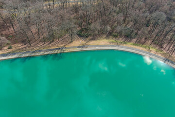 a stunning aerial shot of a gorgeous simmering green lake surrounded by bare and lush green trees...