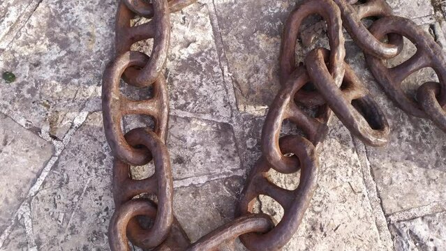 Old rusty iron chain from an anchor laying on the stone floor. Close up of vintage metal heavy duty manacles made of steel in a dungeon or prison cell.