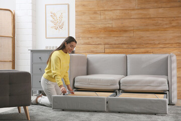 Young woman unfolding sofa into a bed in room. Modern interior - obrazy, fototapety, plakaty