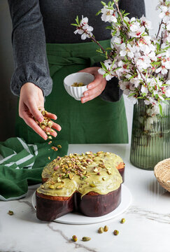 Colomba di Pasqua in the woman shef hands, traditional italian easter dove cake with green pistachio glaze,  fresh spring flowers, pasqua cake