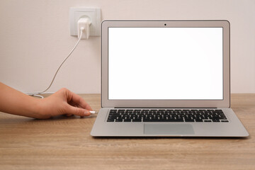 Woman connecting charge cable to laptop on wooden table, closeup. Space for text