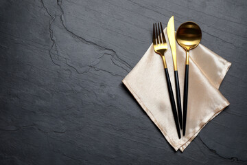 Set of golden cutlery with napkin on black table, top view. Space for text - obrazy, fototapety, plakaty