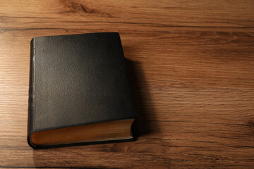 Bible with black cover on wooden table. Space for text