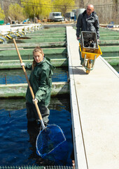 Portrait of man and woman catching with net sturgeon at fish farm