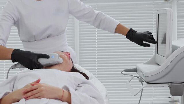 Body massage - young woman having an electric massage procedure on her face and the therapist pointing at the monitor