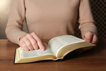 Woman reading Bible at wooden table, closeup