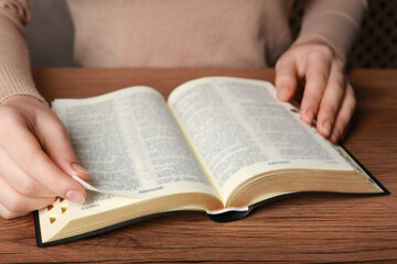 Fototapeta premium Woman reading Bible at wooden table, closeup