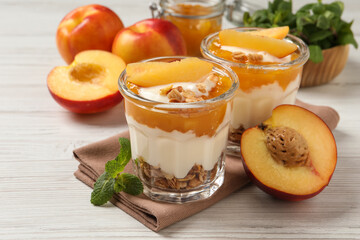 Tasty peach yogurt with granola, pieces of fruit and jam on white wooden table