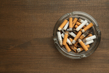 Glass ashtray with cigarette stubs on wooden table, top view. Space for text