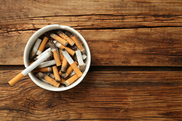 Ceramic ashtray full of cigarette stubs on wooden table, top view. Space for text