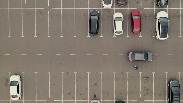 Cars arrive at the parking lot and park in free spaces. Car pass throw the parking lot. Car leaves the parking lot - aerial top overhead drone shot.