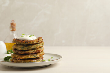 Delicious zucchini pancakes with sour cream served on white wooden table. Space for text