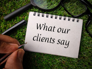 Top view hand holding pen,magnifying glass and glasses with text What our clients say on grass...