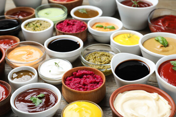 Many bowls with different sauces and herbs on wooden table